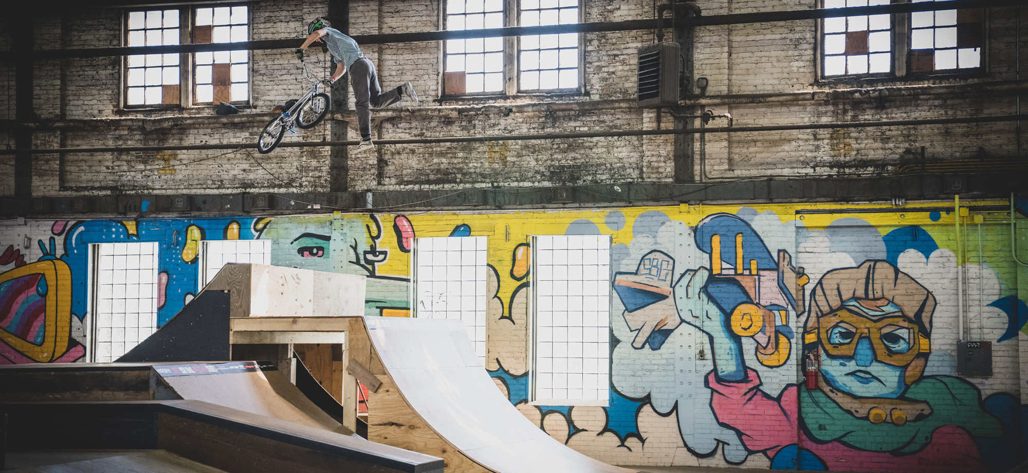 Freestyle bmx rider catching air off a ramp with graffiti wall in the background