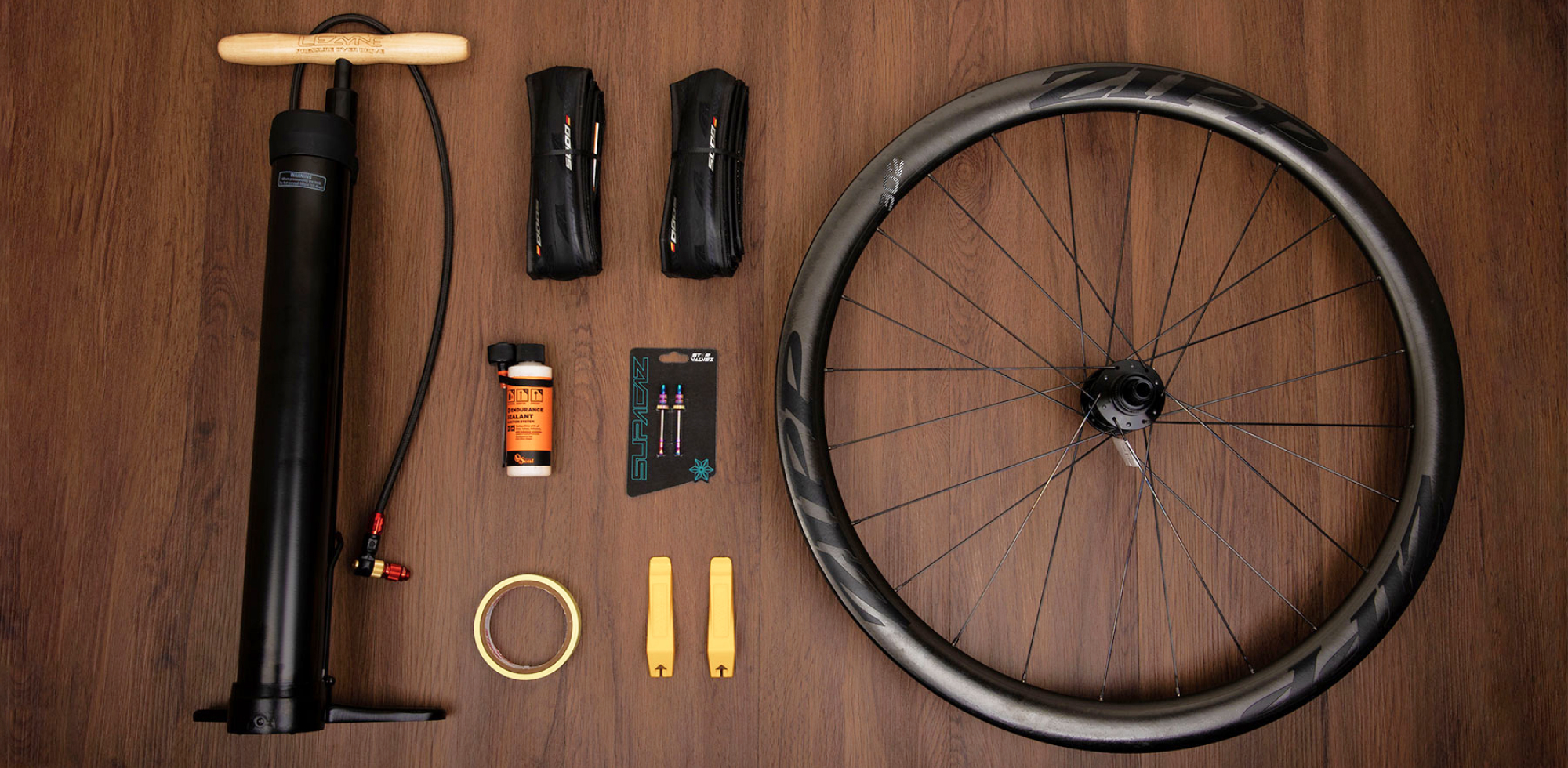 Flat lay image of wheel, tires, floor pump, tire levers, valves, sealant and rim tape