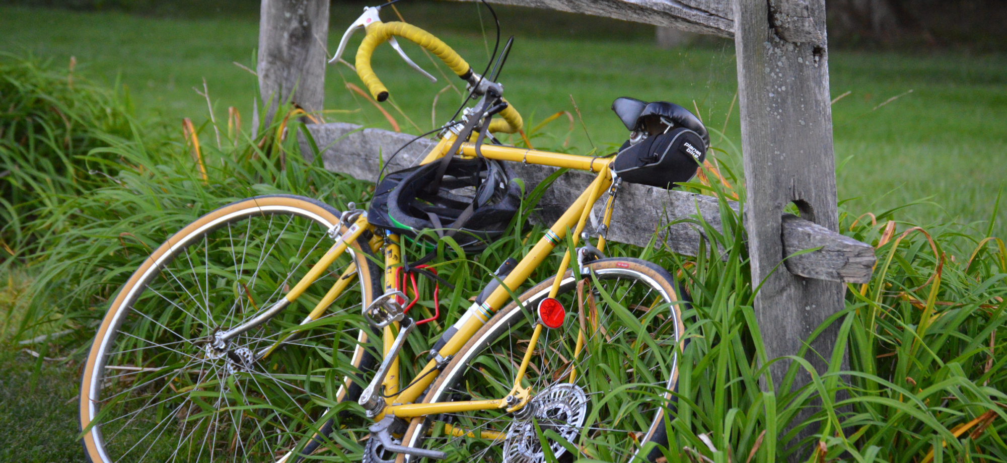 Older yellow bike leaning against a fence