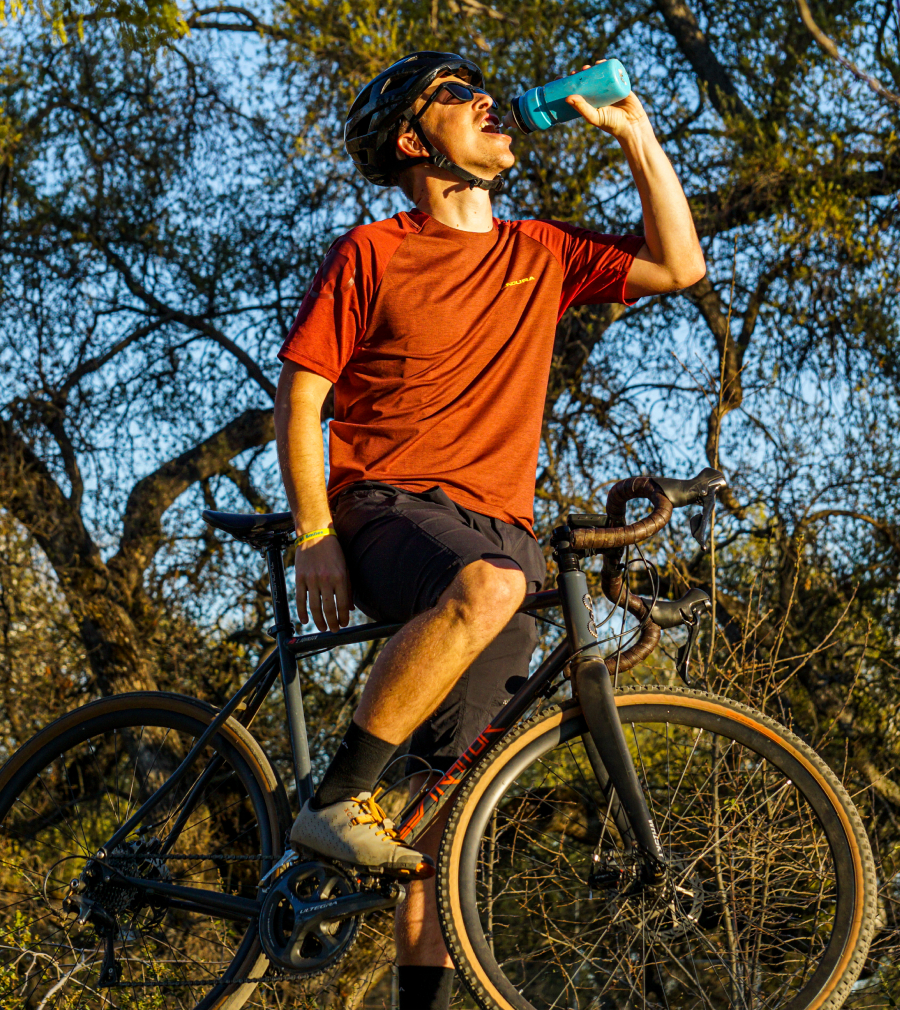 Man drinking from water bottle while standing over gravel bike