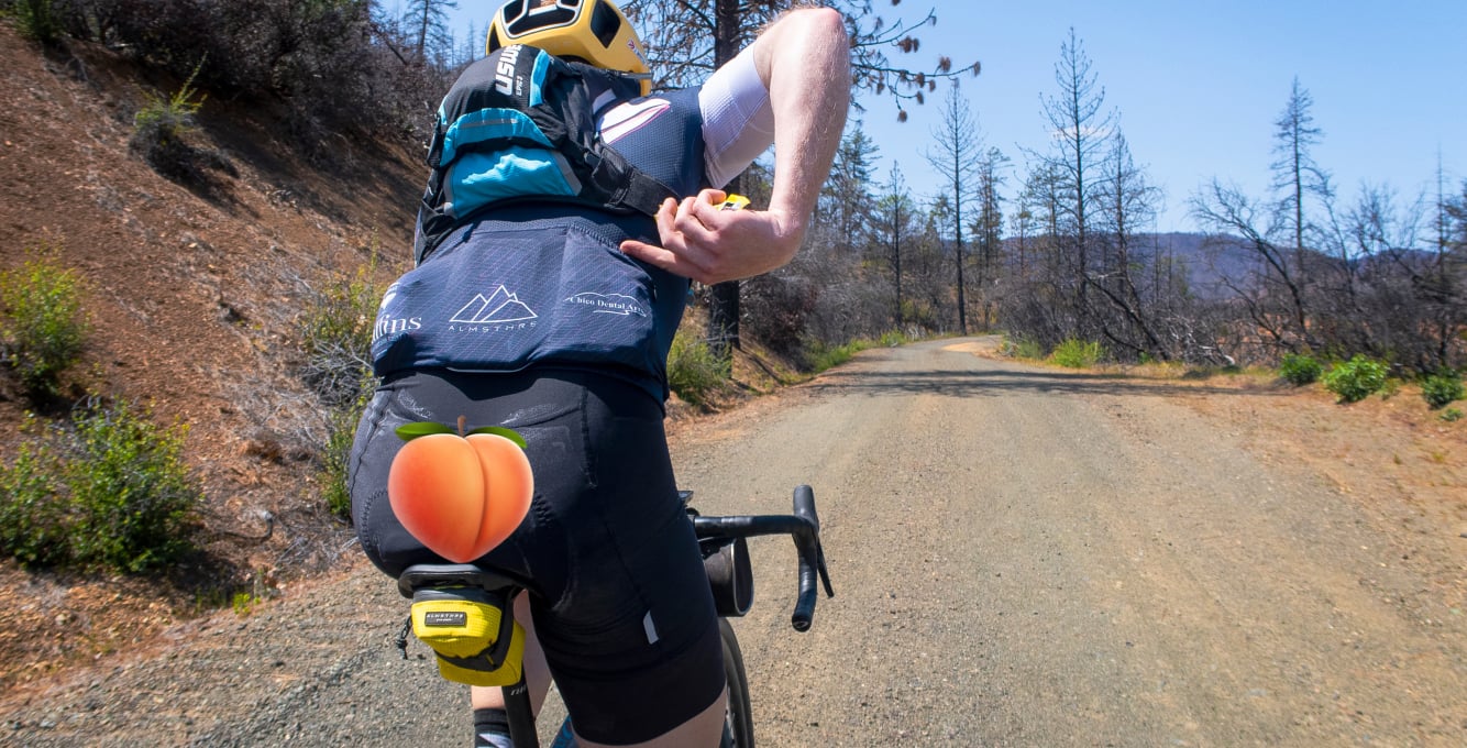 image of gravel cyclist riding with worn out bib pants and a peach emoji added to cover the bad view