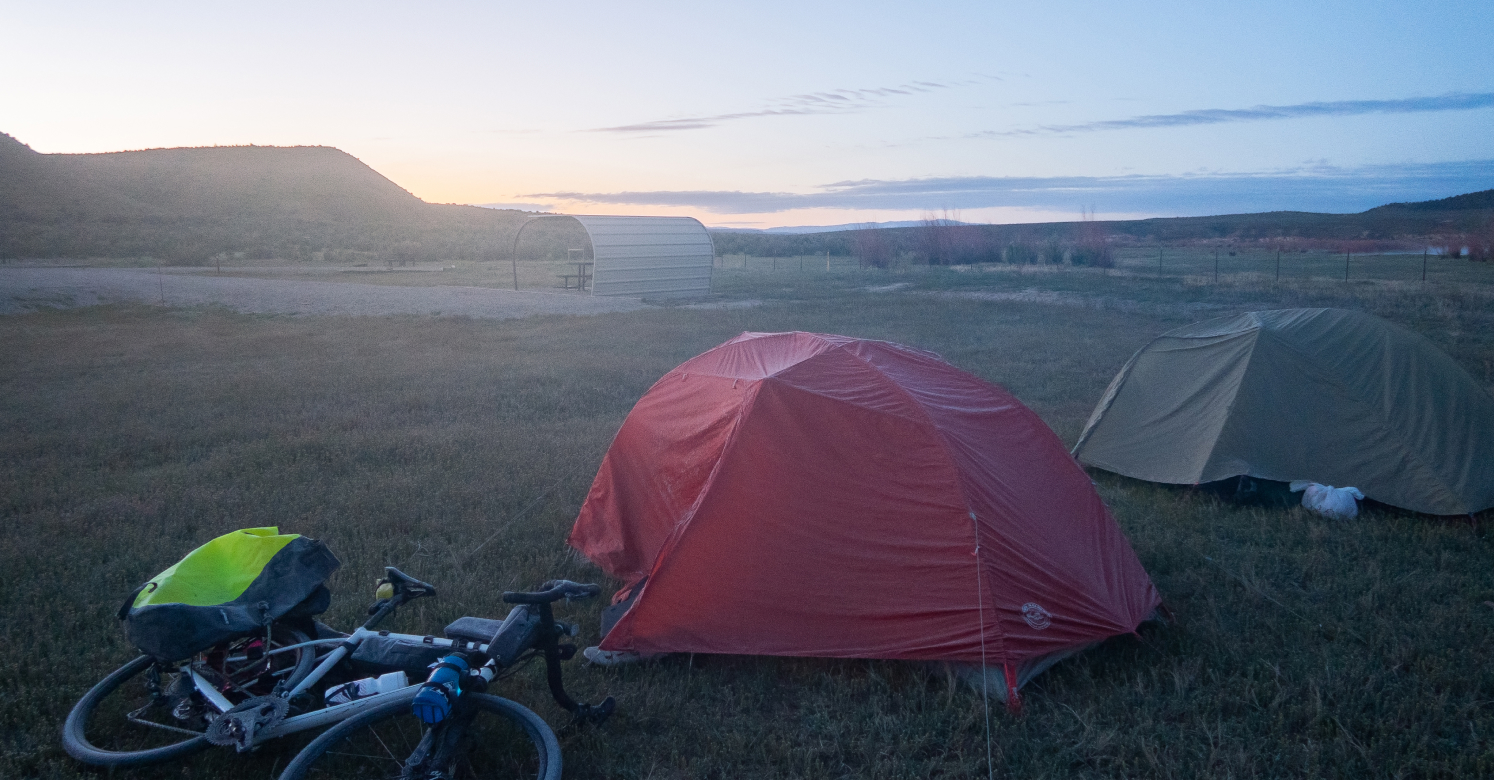 image of touring bike on ground in camp next to two tents